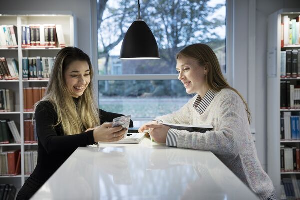 Två studenter tittar på mobil tillsammans. Foto.
