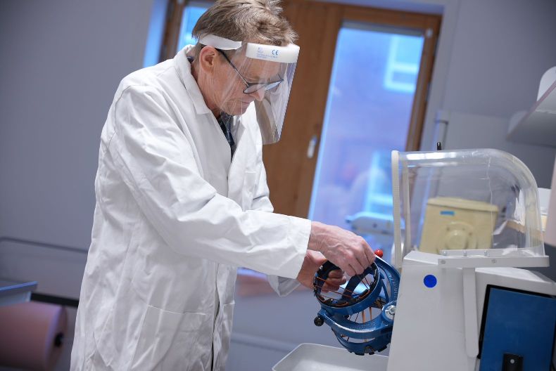 Kyrre Wahlberg in the lab, wearing a safety shield and white coat. Photo.
