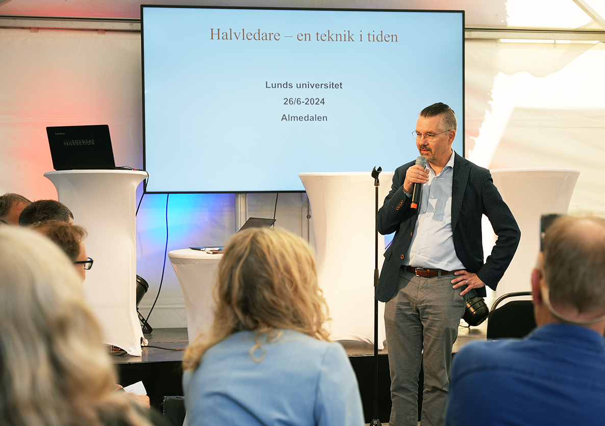 Erik Renström håller i en mikrofon och talar inför en publik. Foto.